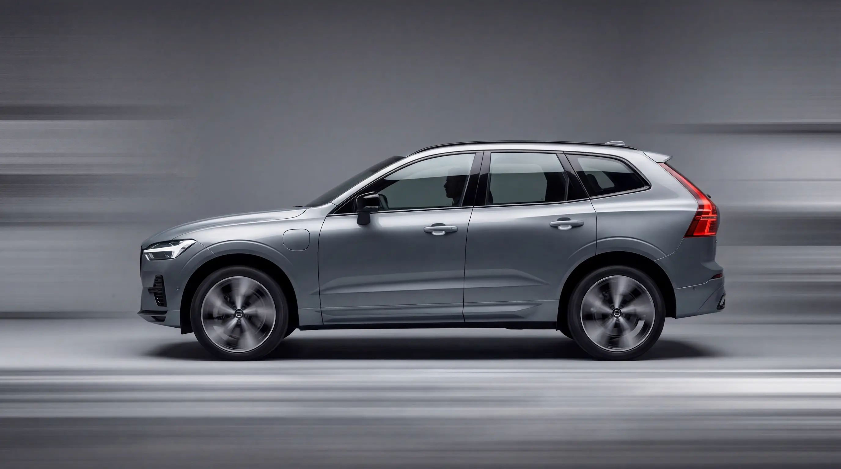 Silver Volvo XC60 SUV driving fast with motion blur against a gray background.